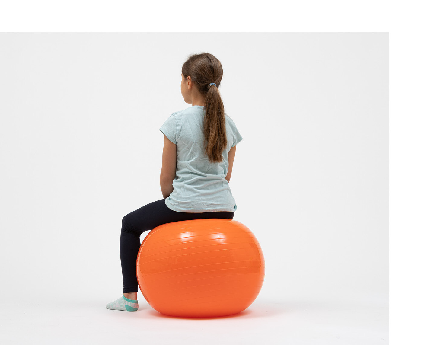 Ein Mädchen sitzt auf einem farbigen, aufgeblasenen Plastikball.