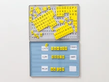 Eine flache, aufklappbare Metallbox, die kleine Magnetblättchen enthält. Alle Magnetblättchen sind mit Buchstaben und Symbolen bedruckt, womit auf dem aufgeklappten Deckel der Box Wörter gelegt werden können.