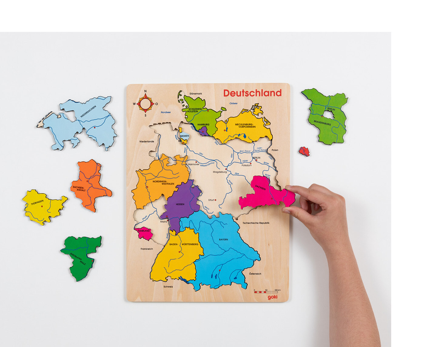 Jemand setzt die Bundesländer Holzteile in die Vorlage des Deutschlandpuzzles an die entsprechende Stelle.