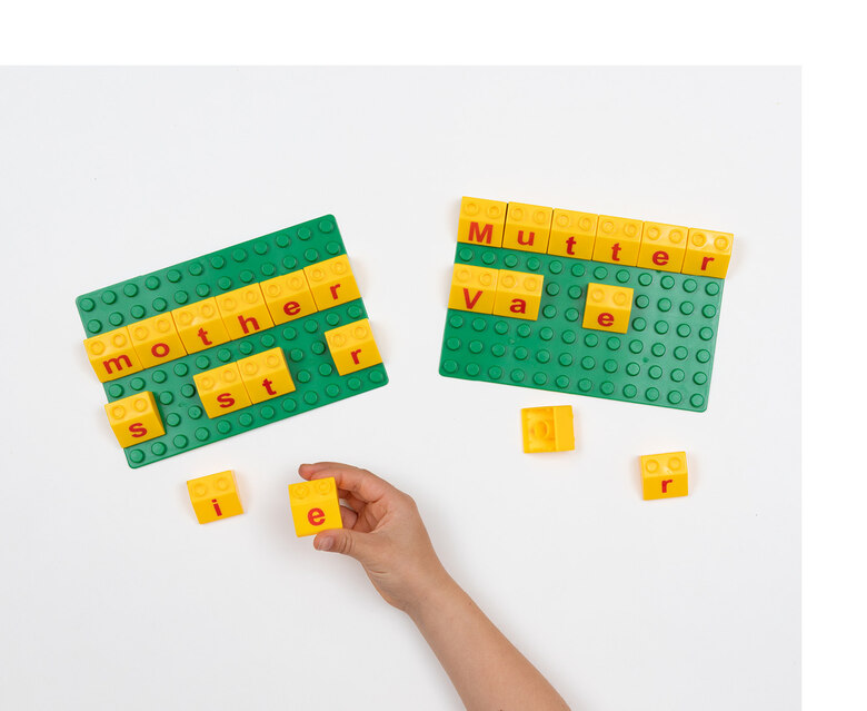 Zwei grüne Platten, auf denen mit gelben Buchstaben-Bausteinen Wörter in deutsch und in englisch gesteckt sind.