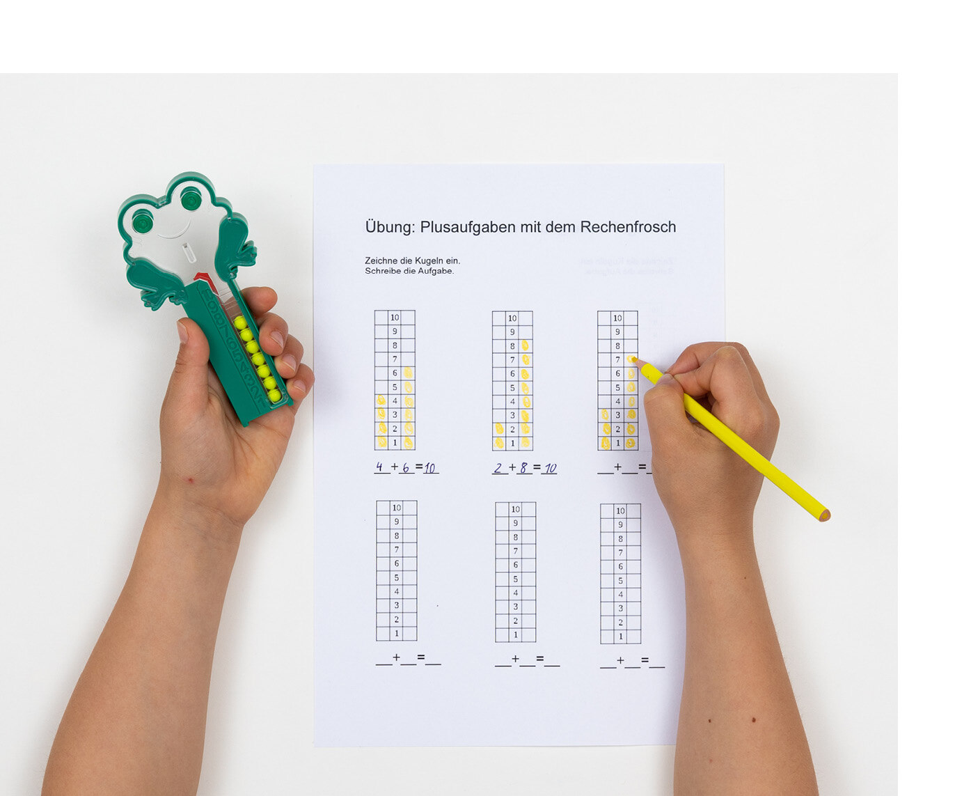 Einer Person hält in der linken Hand den Rechenfrosch und in der rechten Hand einen gelben Bleistift. Vor ihr liegt ein Blatt Papier, auf dem jeweils 10 Rechenaufgaben in 6 senkrecht angeordneten Rechtecken geschrieben stehen.