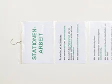 Zwei beschriebene Notizblätter stecken unter einander angeordnet in einer Plastikhülle. Diese Plastikhülle ist an einem Kleiderbügel befestigt.