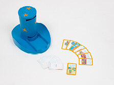 Ein kleiner, blauer Plastik-Zylinder mit Schlitzen am oberen und unteren Ende des Zylinders, steht auf einem Tisch. Daneben liegen bunte verdeckte und aufgedeckte Spielkarten.