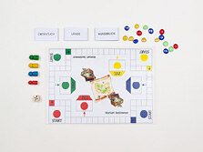 Ein Spielfeld mit verschiedenen Feldern. Daneben Spielfiguren, ein Würfel und Karten mit Wörtern darauf.